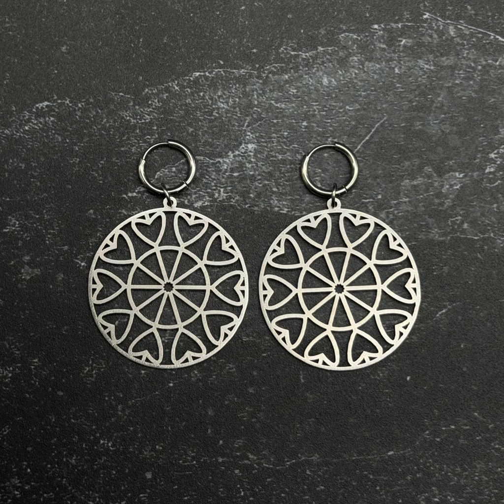 Stainless steel heart mandala earrings with intricate designs on a textured black background