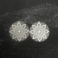 Stainless steel floral mandala earrings with intricate designs on a textured black background