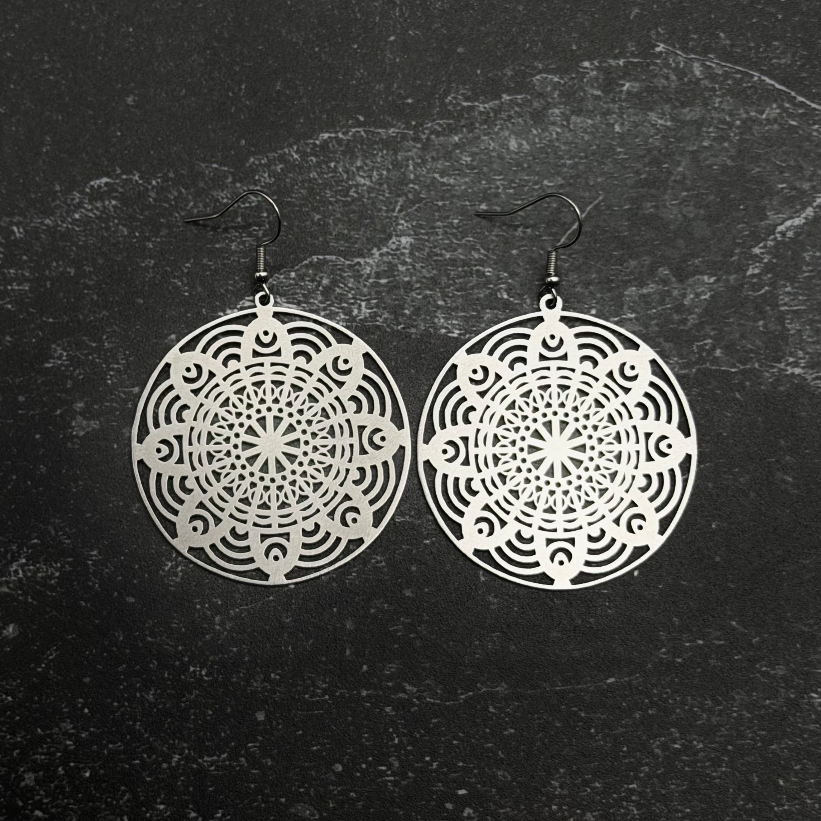 Stainless steel floral mandala earrings with intricate designs on a textured black background