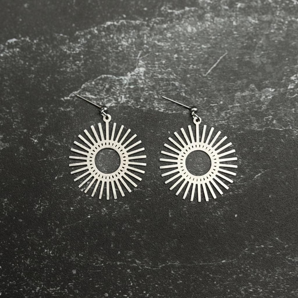 Stainless steel sun design earrings on dark surface. 