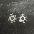 Stainless steel sun design earrings on dark surface. 