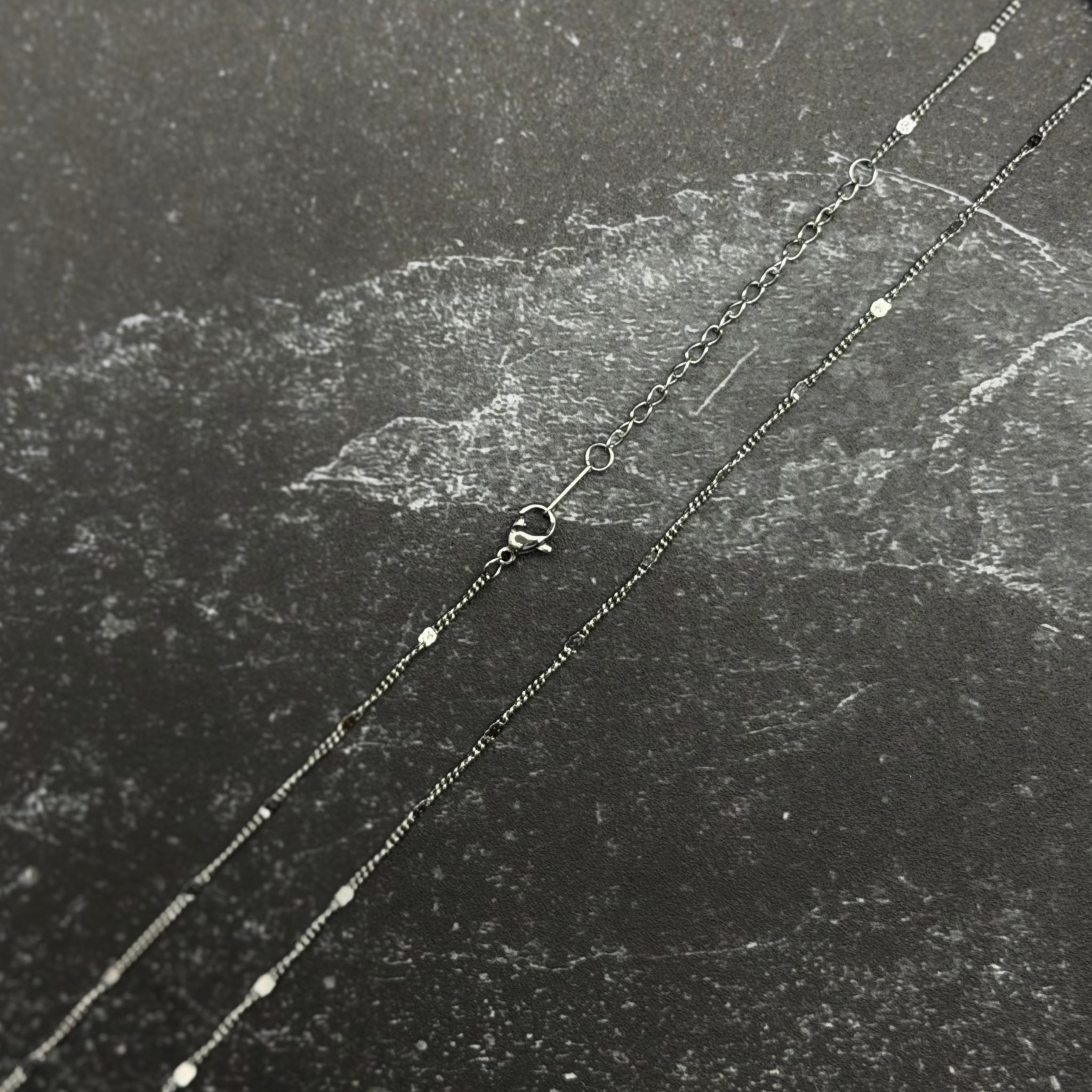 Stainless steel chain with lobster clasp on dark surface