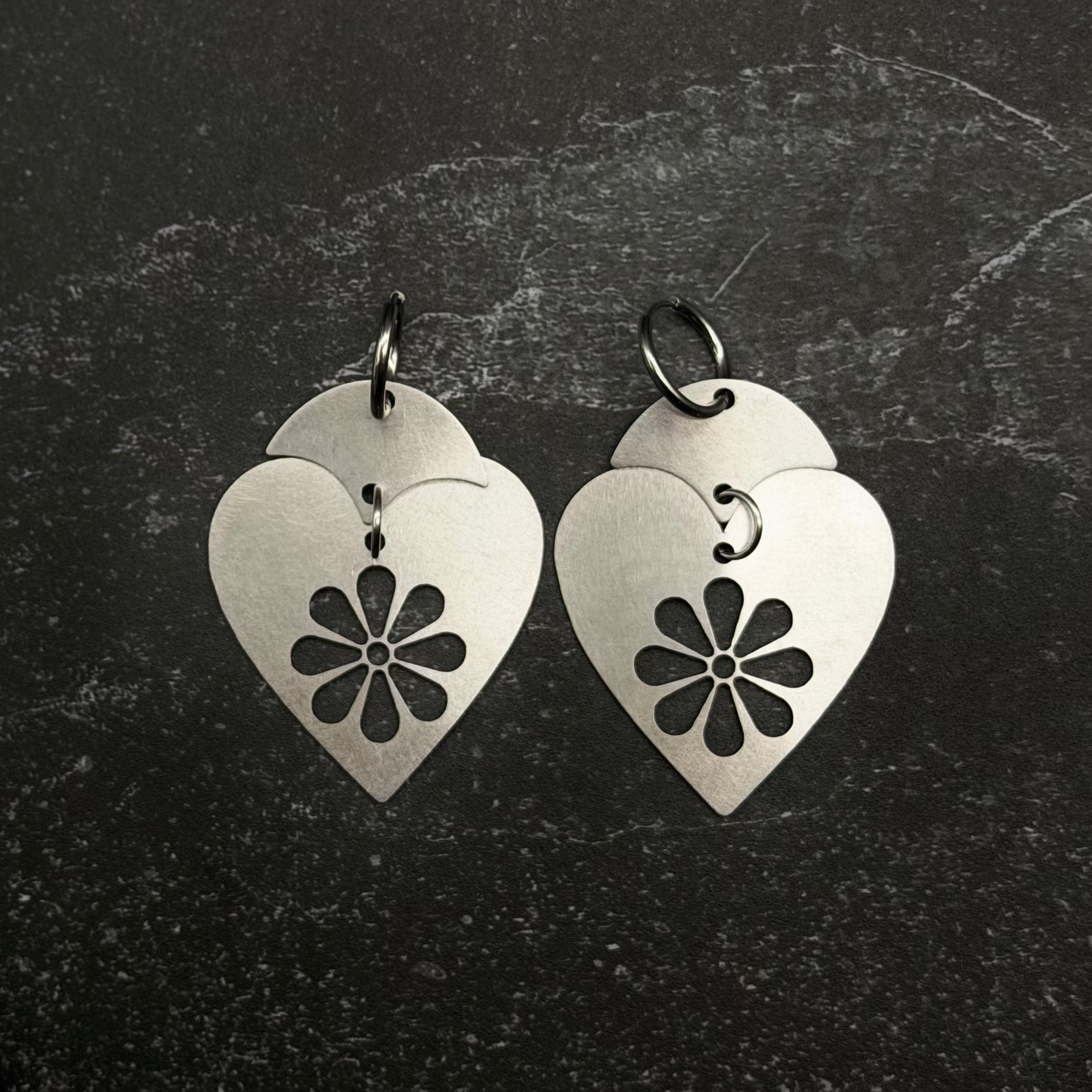 Stainless steel Heart-shaped earrings with floral design on a dark textured background