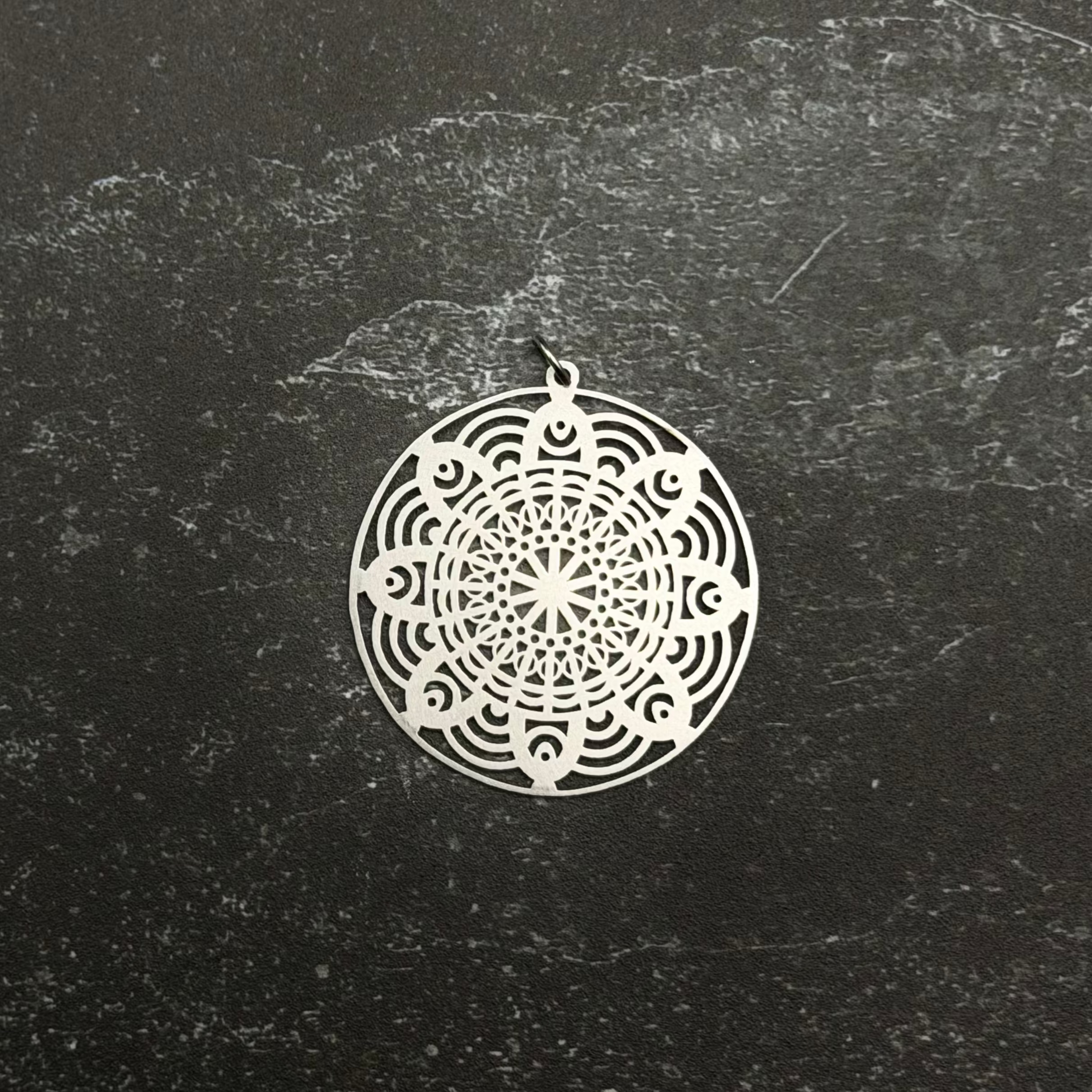 Stainless steel mandala pendant on a black textured surface