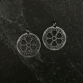 Pair of silver leaf mandala earrings on a black stone surface