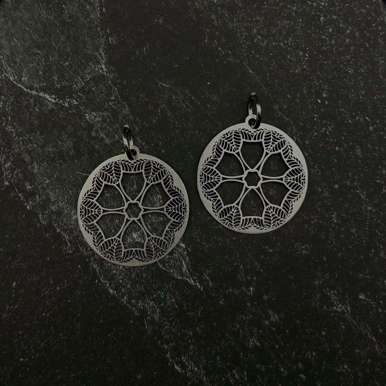 Pair of silver leaf mandala earrings on a black stone surface