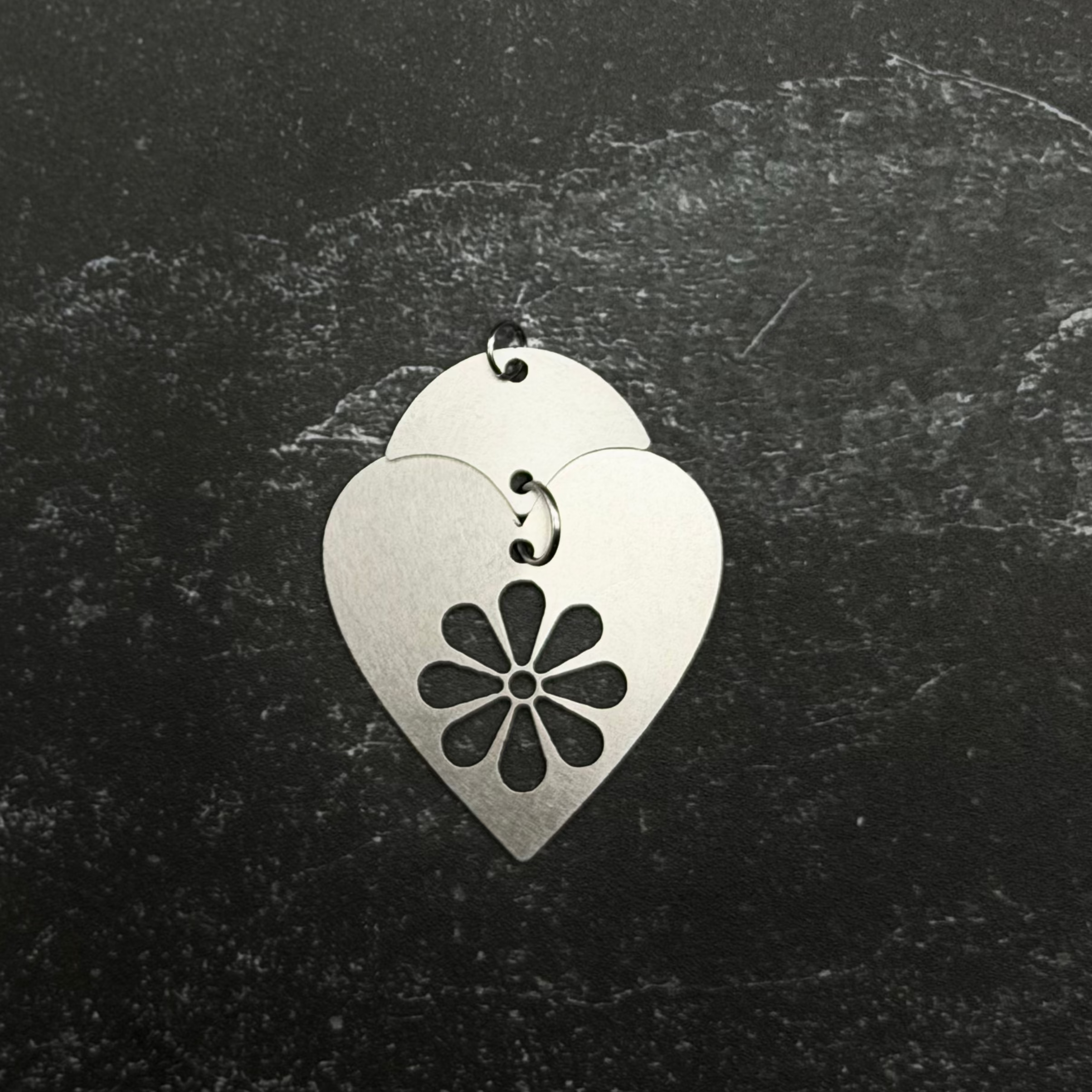 Stainless steel heart-shaped pendant with a floral design on a dark textured background