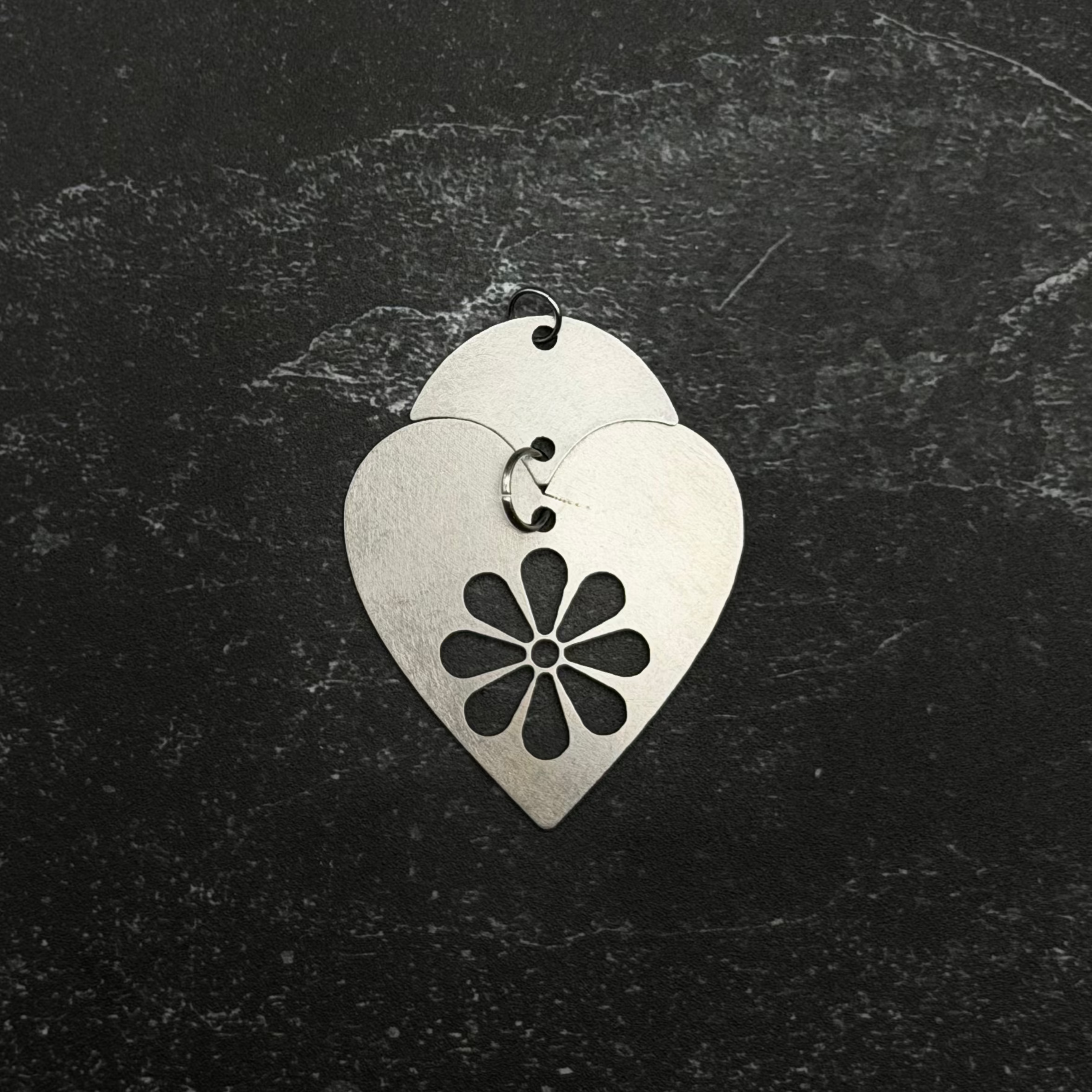 Stainless steel heart-shaped pendant with floral design on a dark textured background
