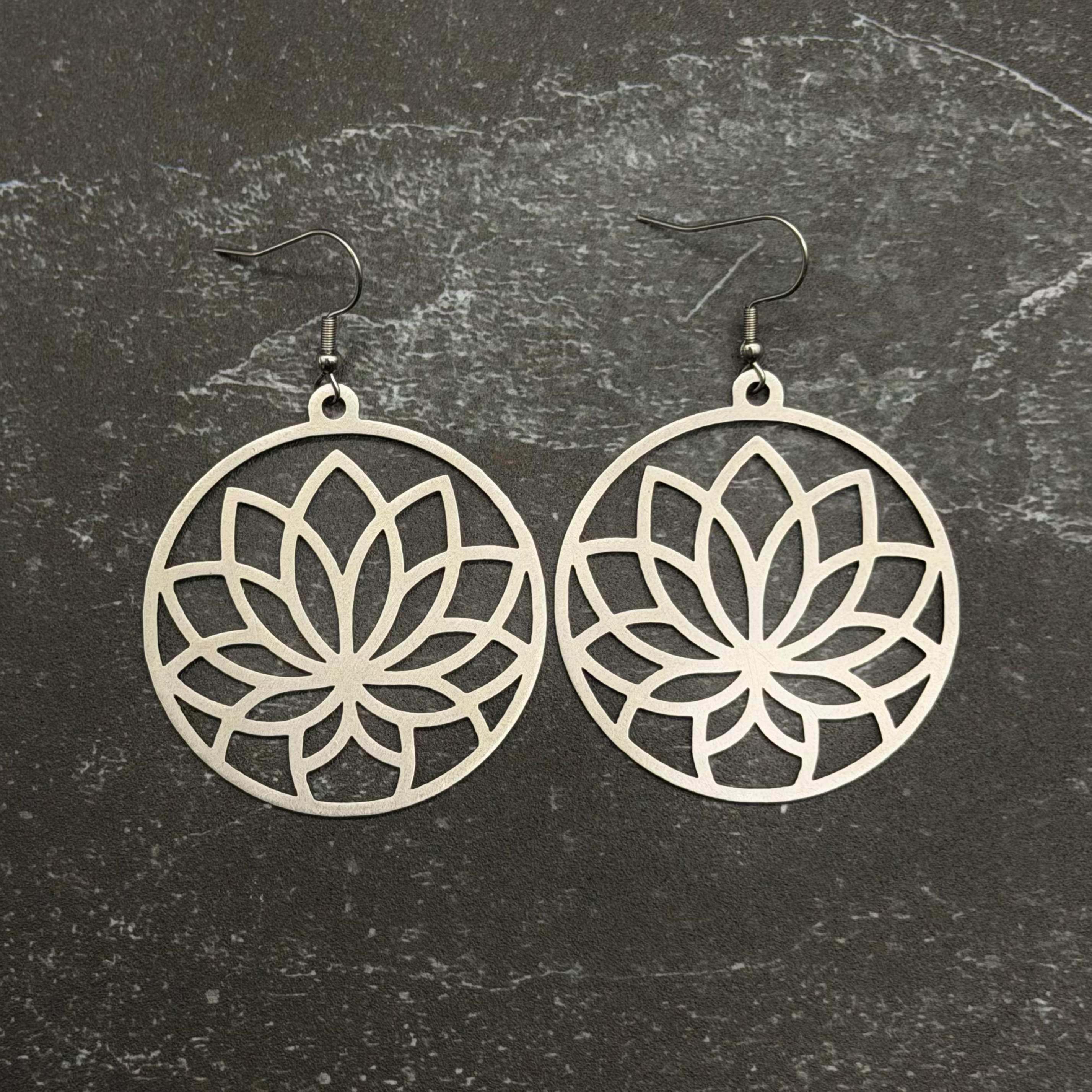 Stainless steel lotus earrings with intricate designs on a textured black background