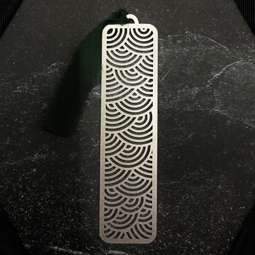 Stainless steel bookmark with surge wave pattern on a black surface