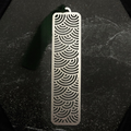 Stainless steel bookmark with surge wave pattern on a black surface