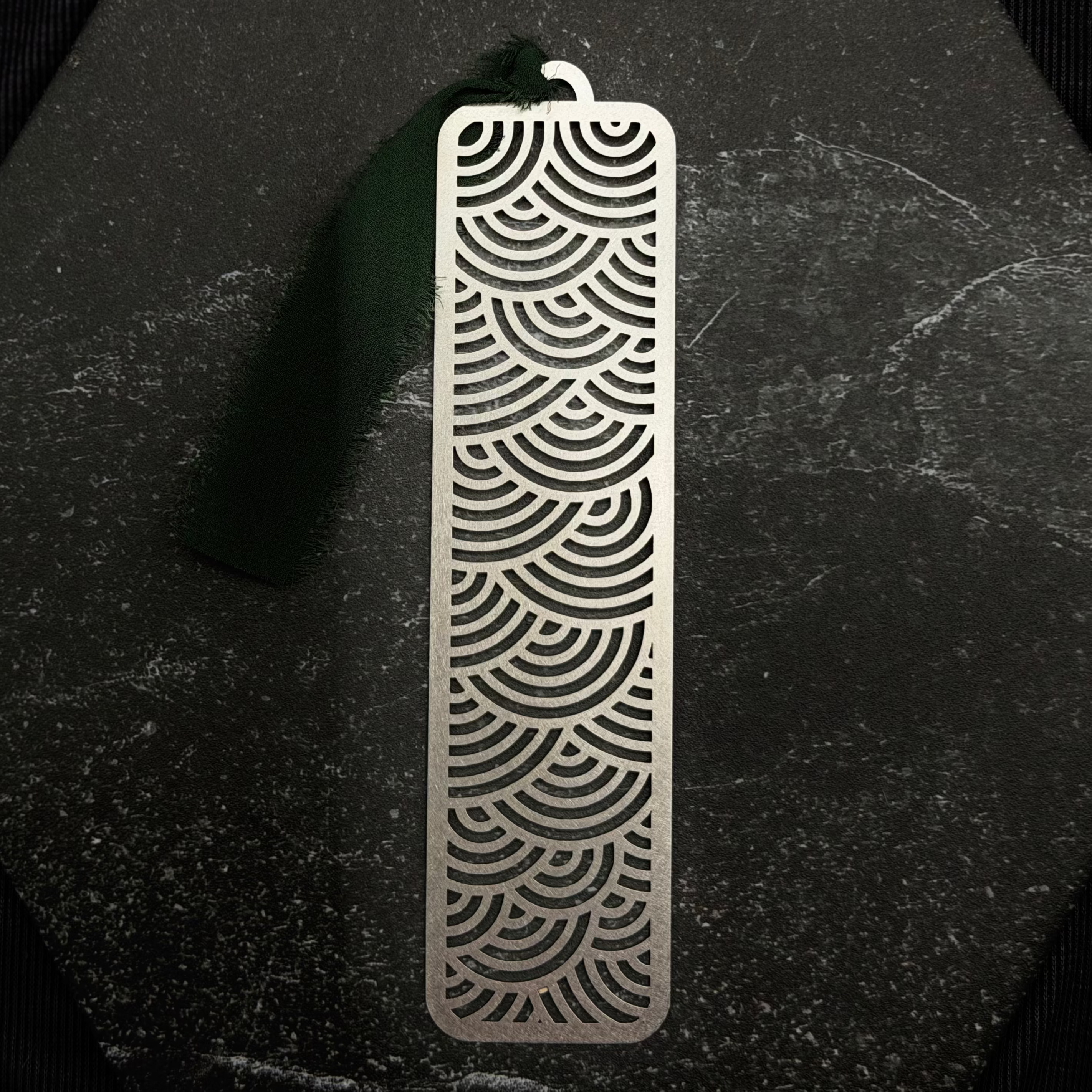 Stainless steel bookmark with surge wave pattern on a black surface