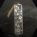 Stainless steel bookmark with floral patterns on a dark surface