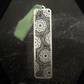 Stainless steel floral bookmark with intricate patterns on a black surface