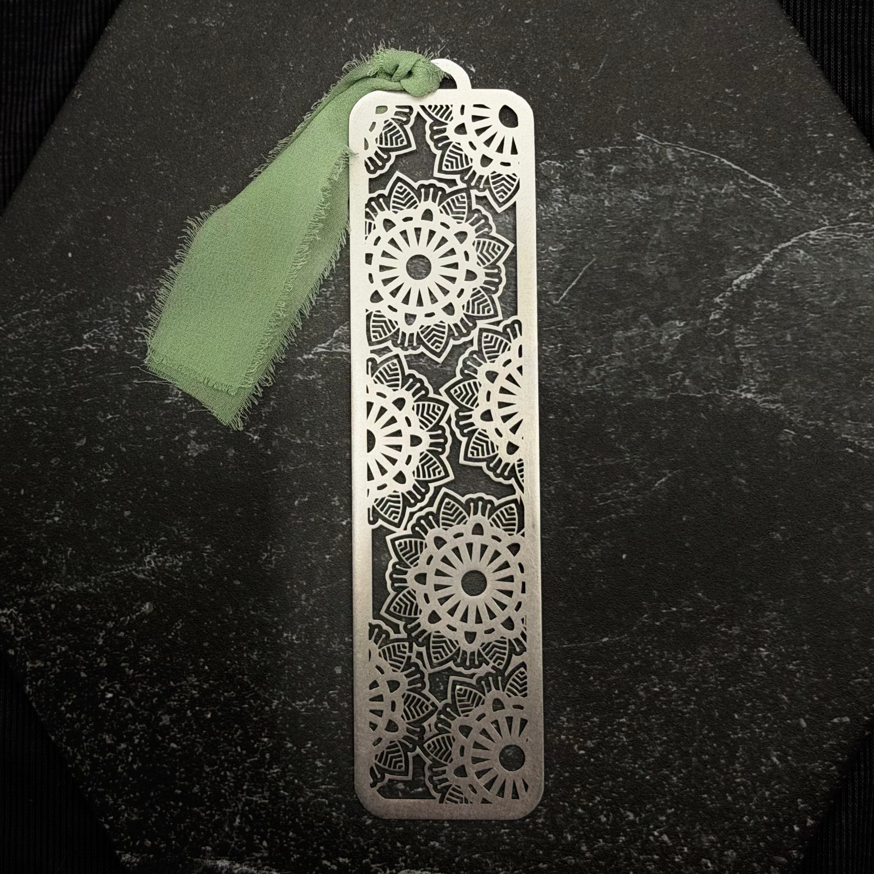 Stainless steel floral bookmark with intricate patterns on a black surface