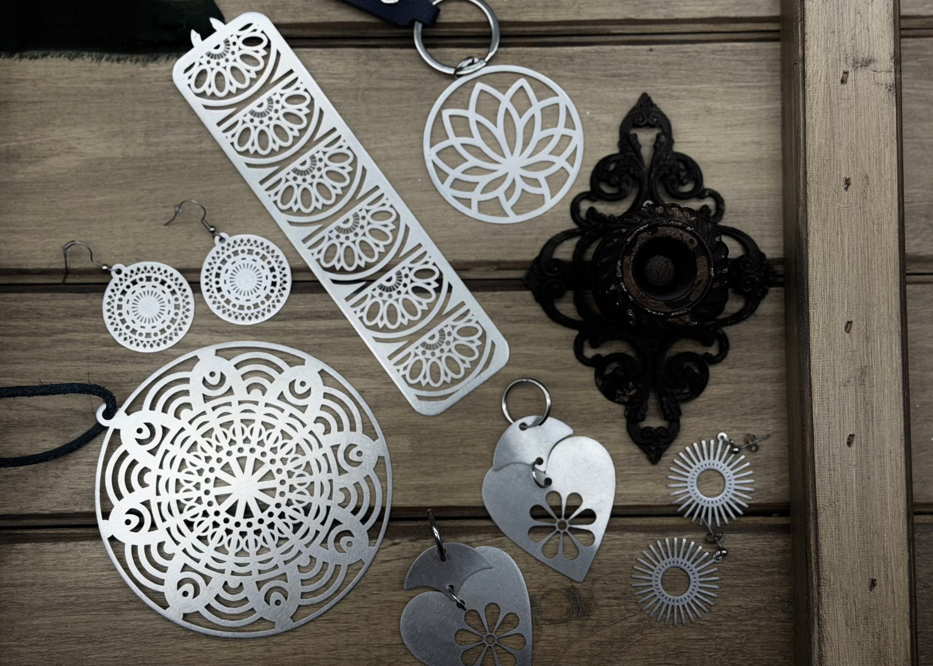 Handcrafted stainless steel mandala pendants and geometric earrings on a rustic wood background.