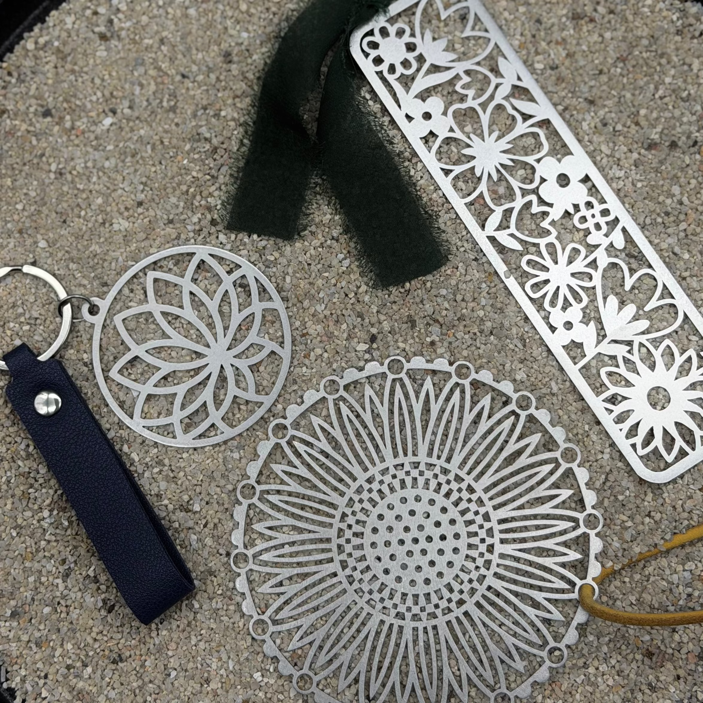 Decorative metal keychains, decorative ornament, and a ruler on a sandy surface.
