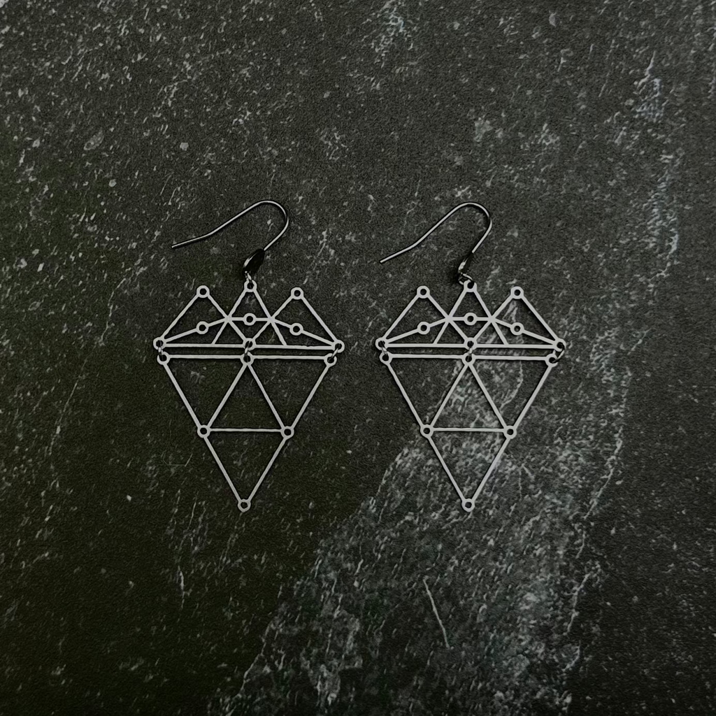 Geometric earrings on a dark stone surface.