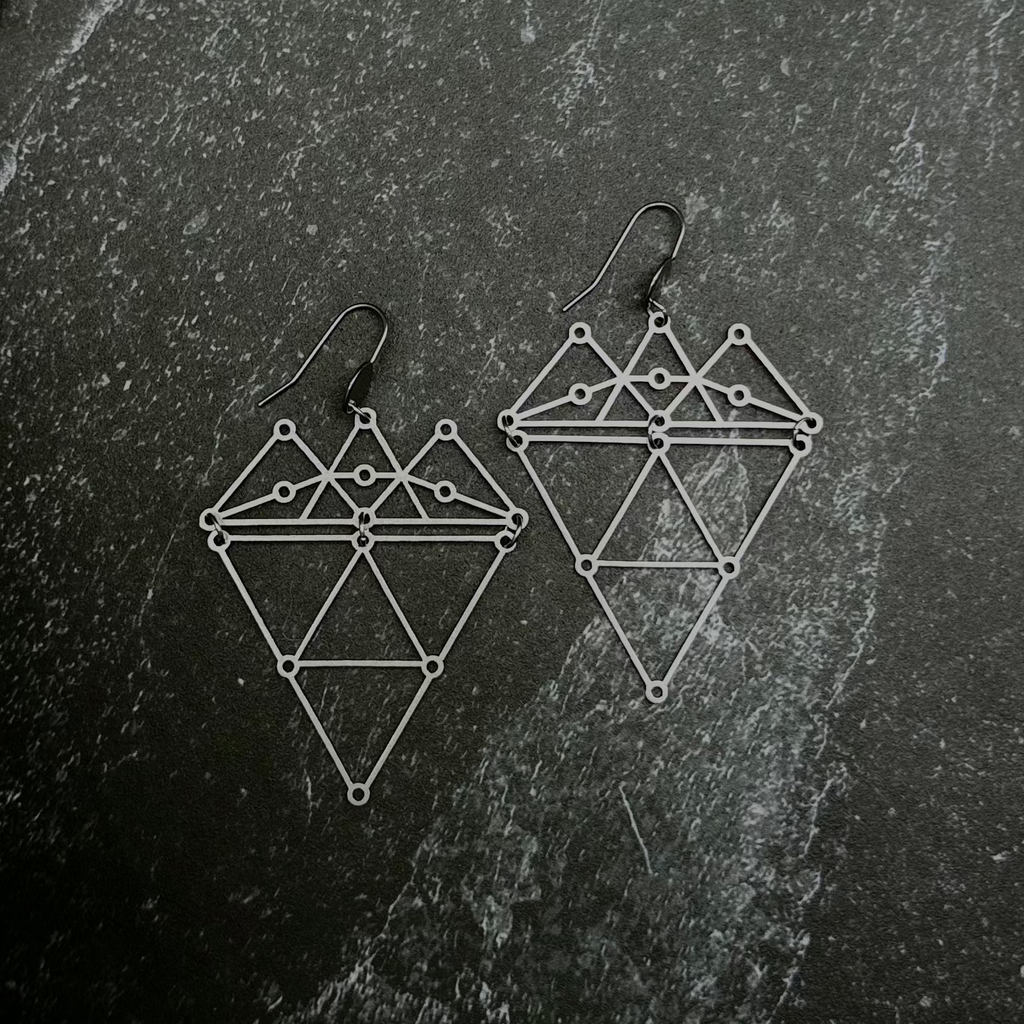 Geometric earrings on a dark stone surface.