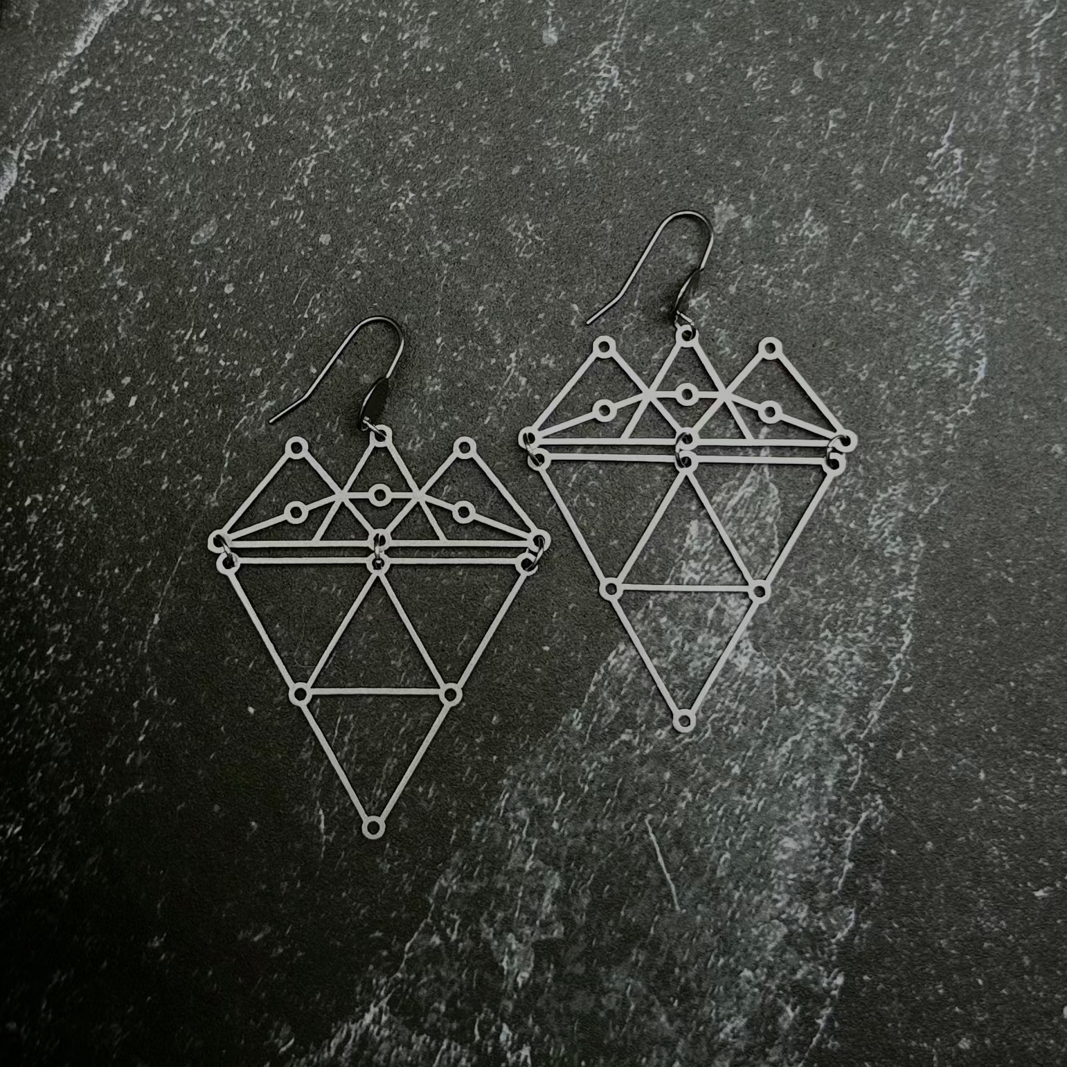 Geometric earrings on a dark stone surface.