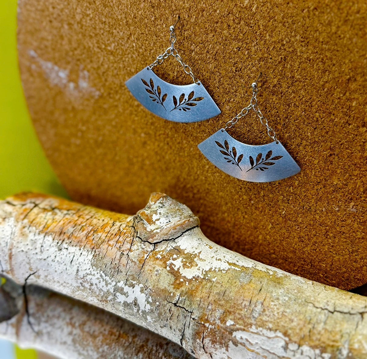 Silver leaf-patterned earrings hanging on a wooden surface with a brown background