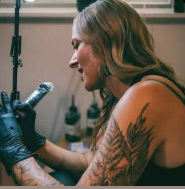 Person with tattoos holding a tattoo machine in a tattoo studio.