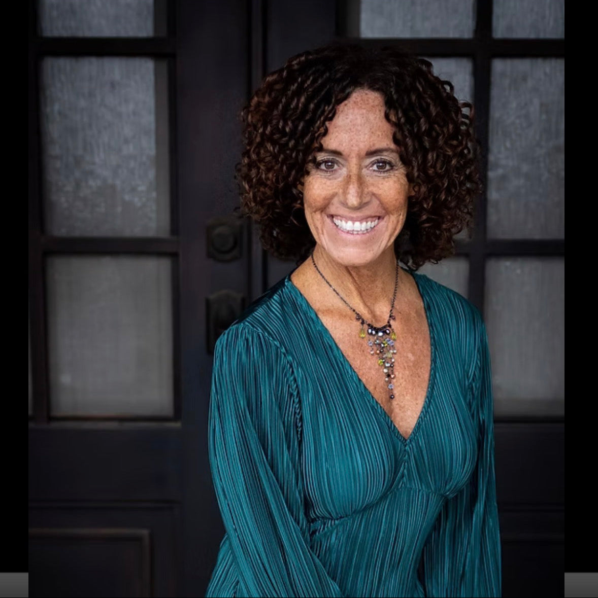 Woman wearing a teal blouse sitting against a dark background