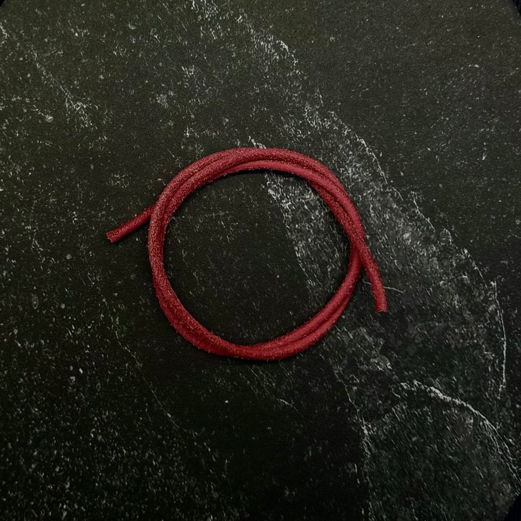 A close-up of a black fabric garment with a dark hexagonal patch or panel, featuring a coiled red cord or strap resting on top.