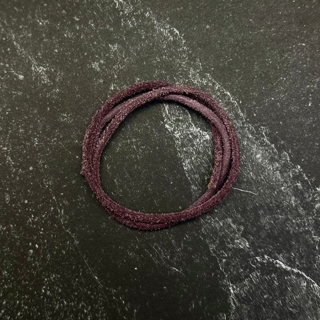 A dark burgundy braided hair tie or elastic band displayed on a hexagonal dark stone slab, set against a dark black fabric background.