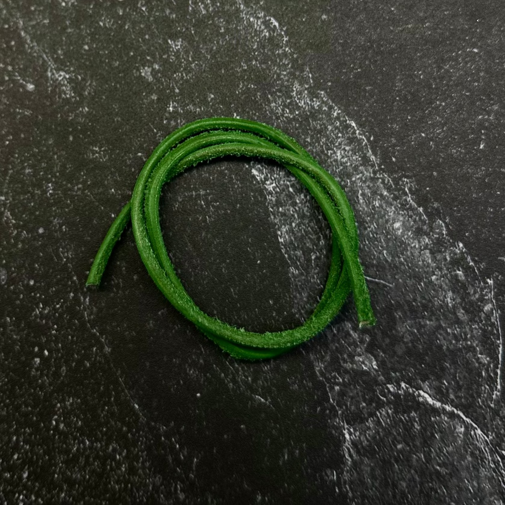 A bright green braided cord or strap coiled on a dark hexagonal stone slab, set against a dark navy fabric background.
