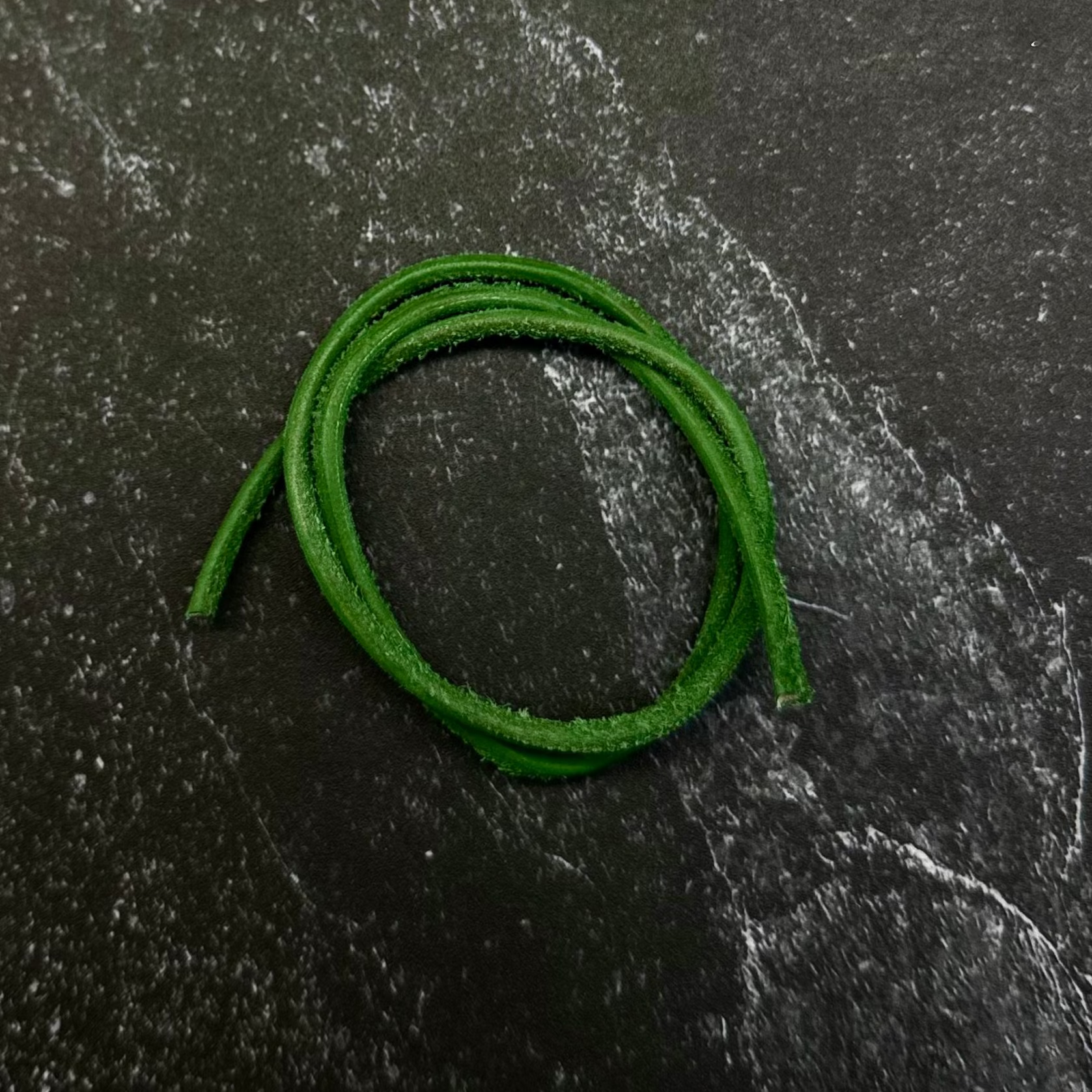 A bright green braided cord or strap coiled on a dark hexagonal stone slab, set against a dark navy fabric background.