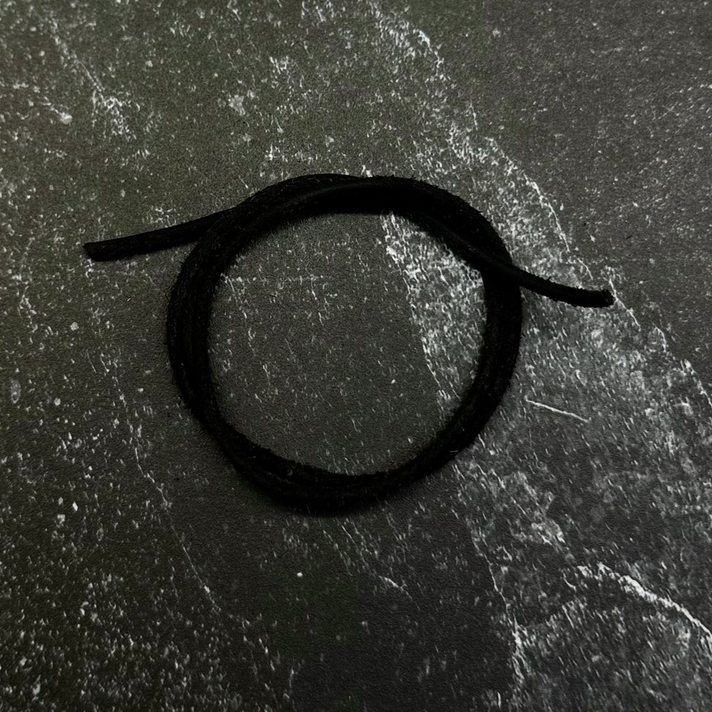 A close-up of a dark hexagonal patch or emblem with a black circular symbol, placed on a dark navy fabric background.