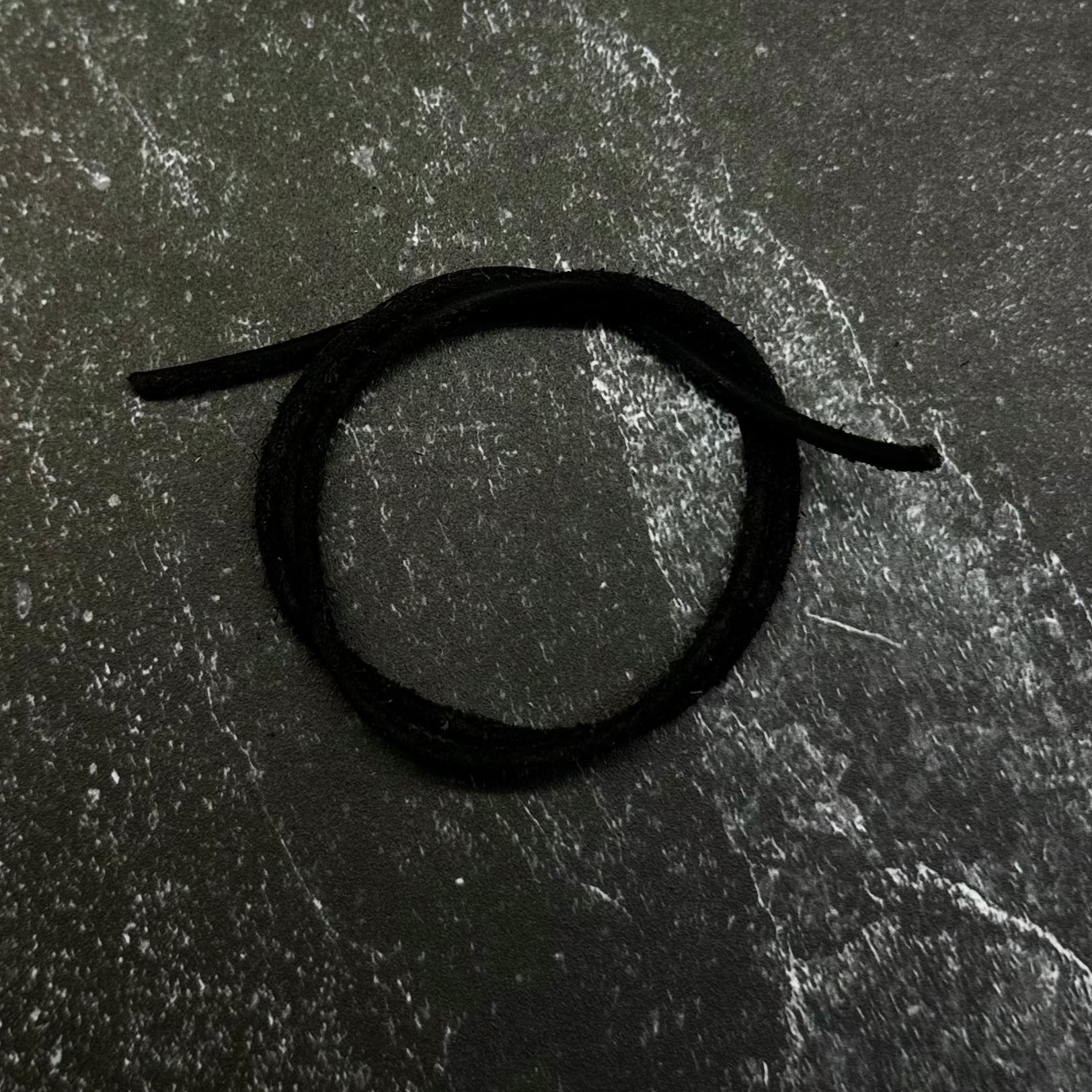 A close-up of a dark hexagonal patch or emblem with a black circular symbol, placed on a dark navy fabric background.