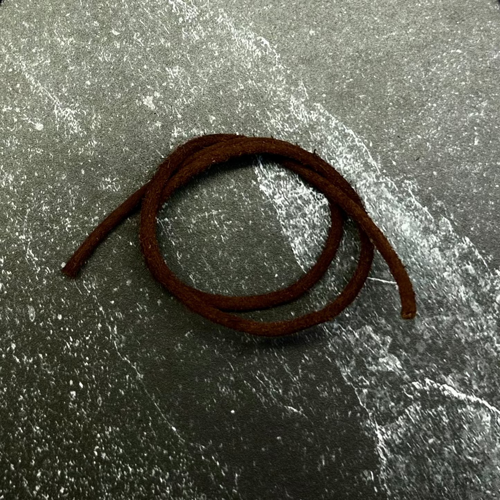 A dark brown braided cord or strap coiled on a hexagonal gray stone slab, set against a dark charcoal gray fabric background.