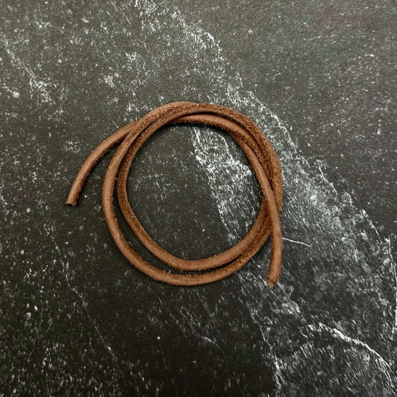 A coiled brown leather cord or strap resting on a dark hexagonal stone slab, placed on top of a black fabric background.