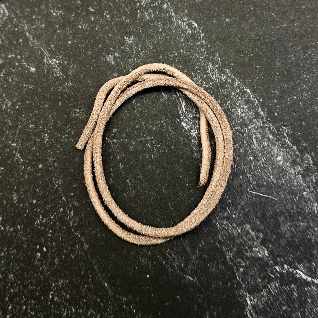 A beige braided cord or strap coiled on a dark hexagonal stone slab, set against a black fabric background.