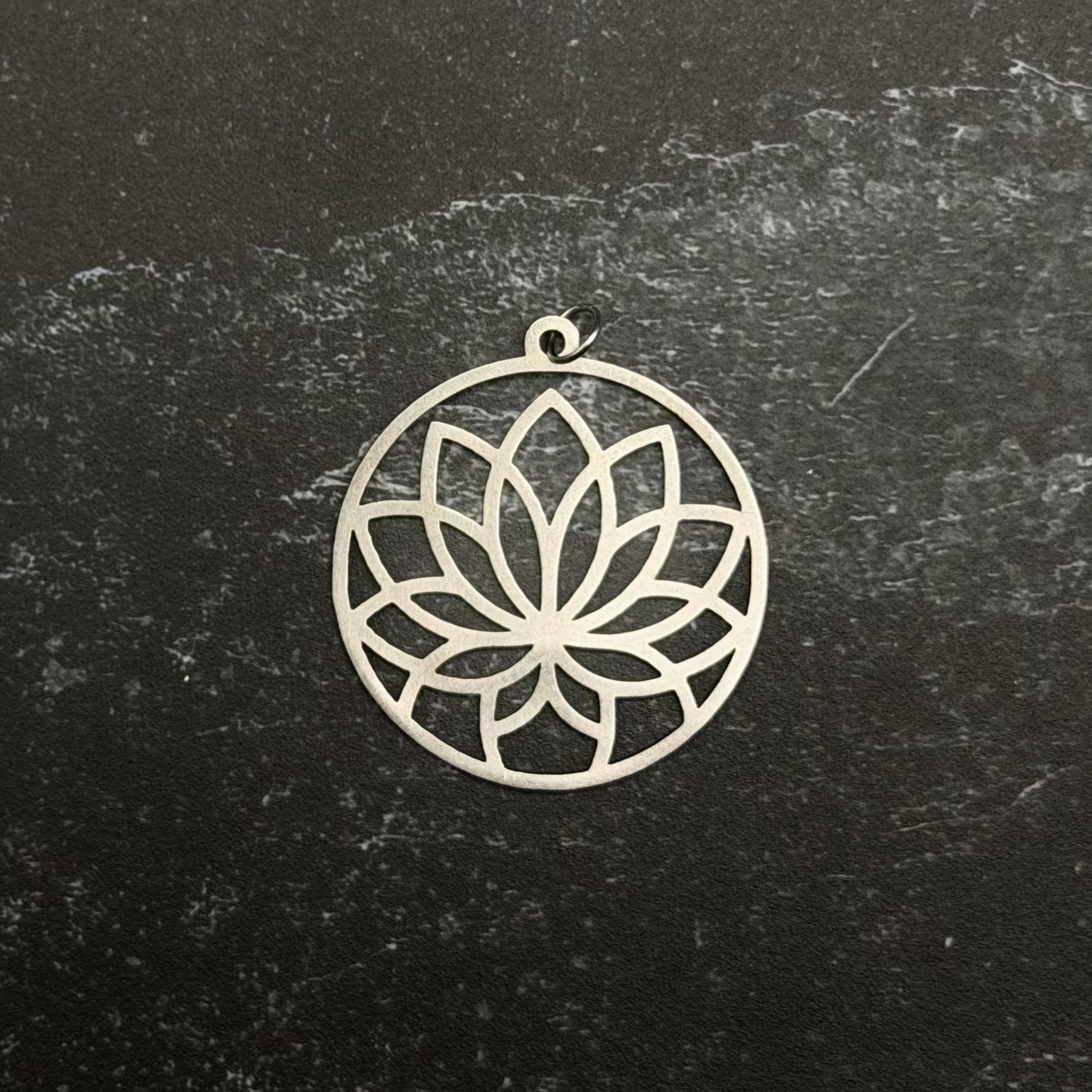 Stainless steel lotus pendant on a black stone surface