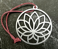 A silver metal lotus pendant with a red cord, displayed on a dark hexagonal stone slab over a black fabric background.