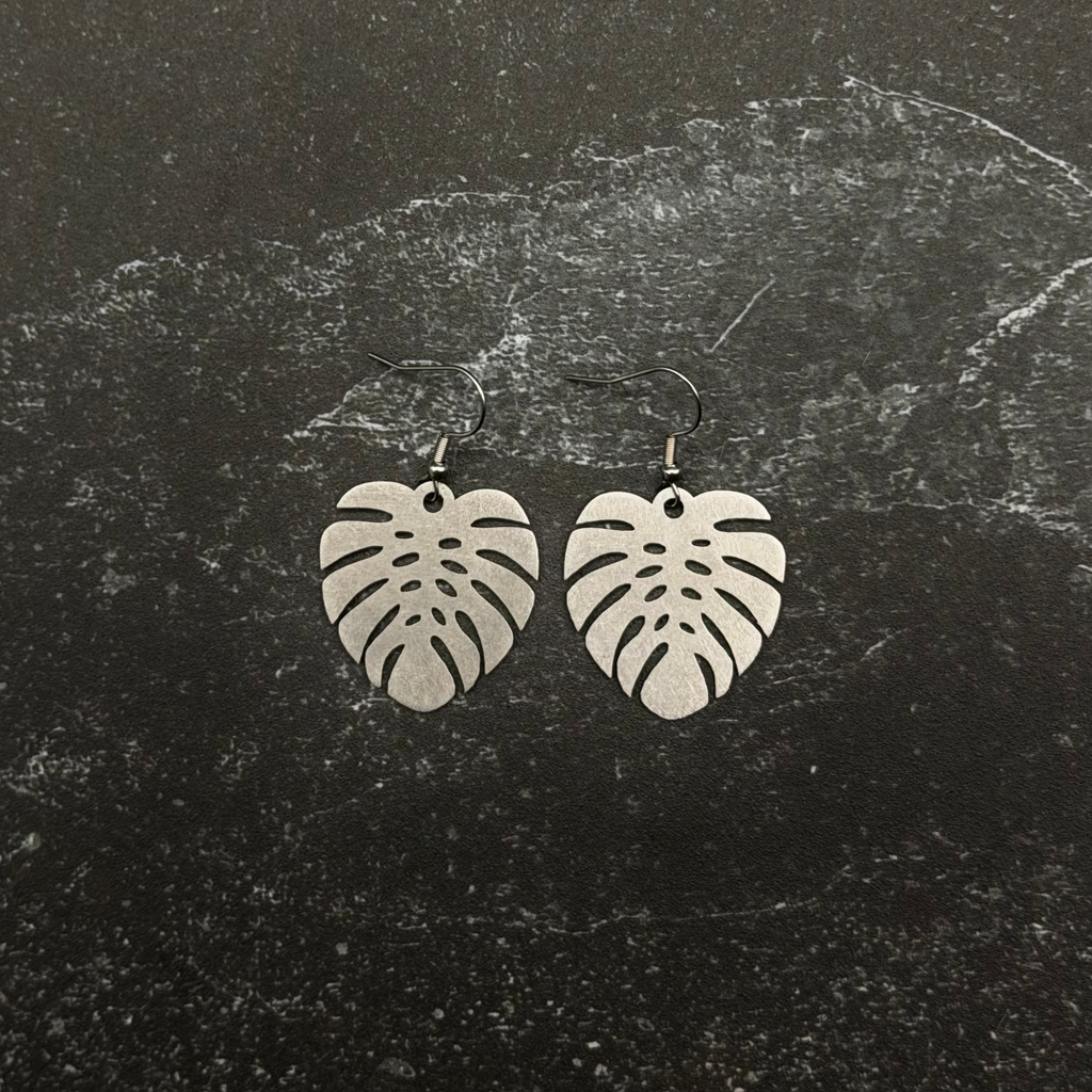 Stainless steel Large monstera earrings on a dark textured surface