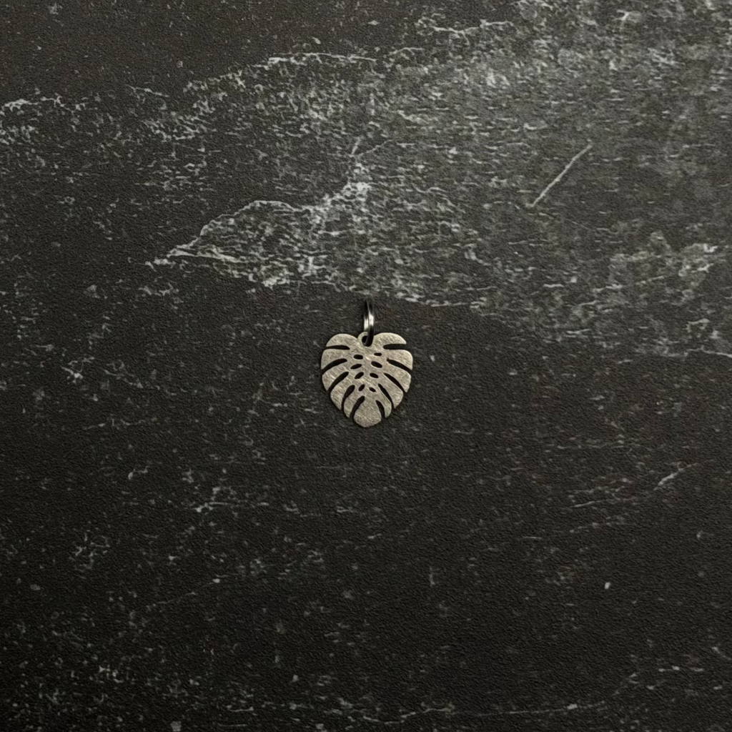 Stainless steel small monstera pendant on a textured black surface