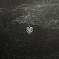 Stainless steel small monstera pendant on a textured black surface