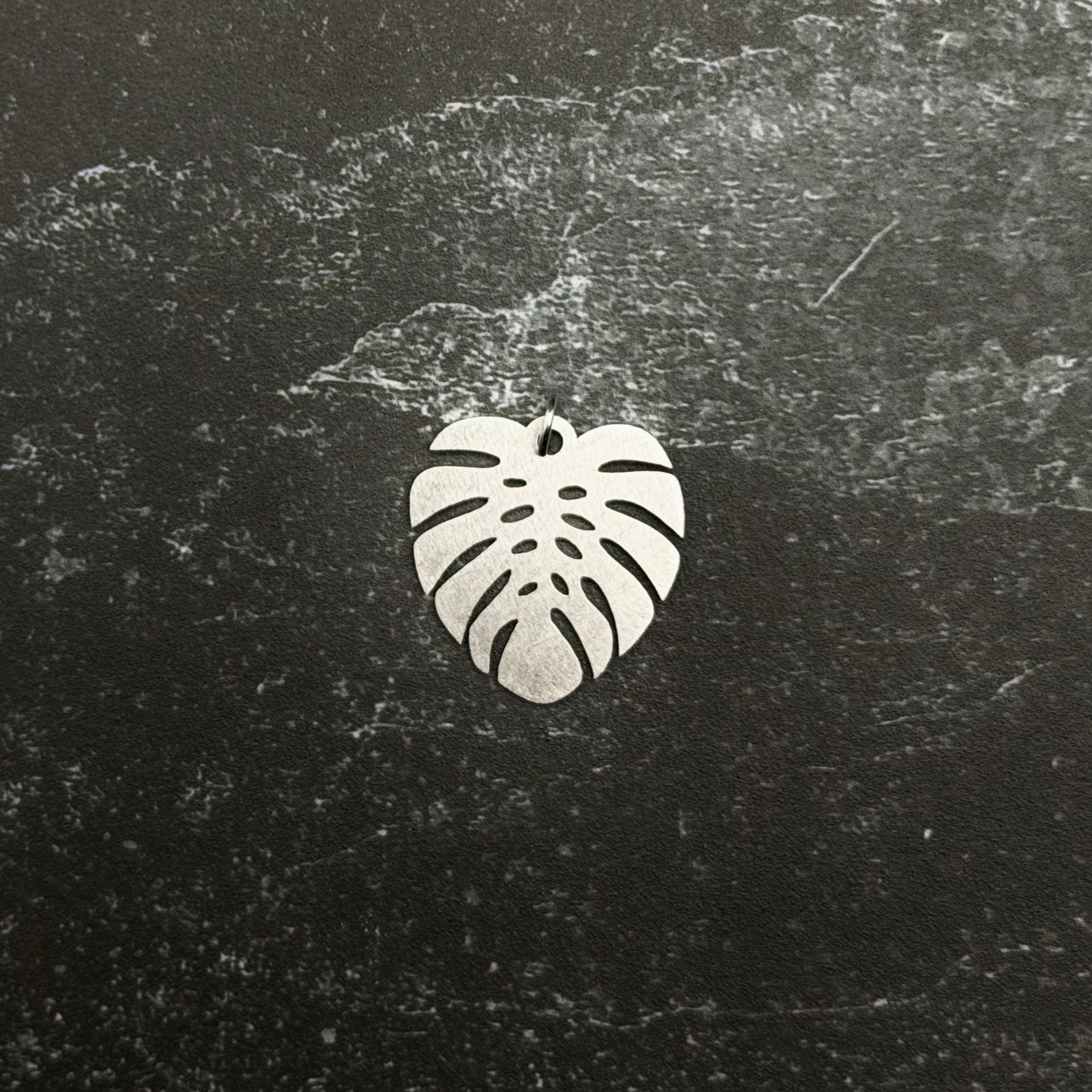 Stainless steel large monstera pendant on a dark textured surface
