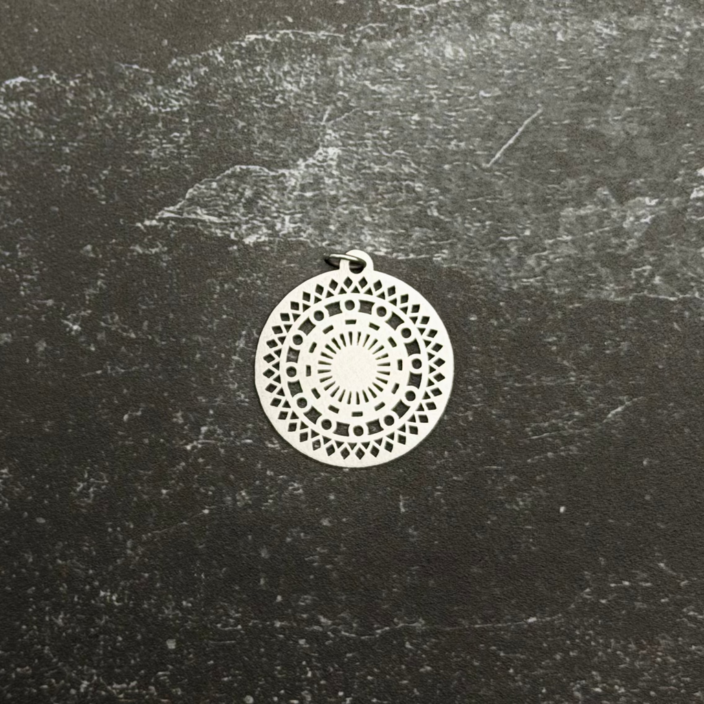 Stainless steel mosaic pendant with intricate design on a textured black surface