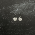 Stainless steel Small monstera earrings on a textured black surface