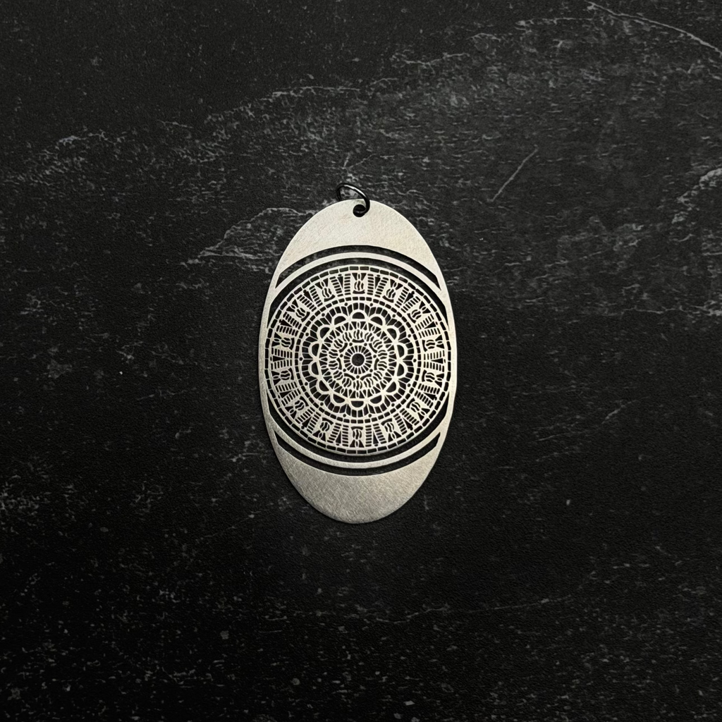 Stainless steel Oval-shaped pendant with intricate black pattern on a dark textured background