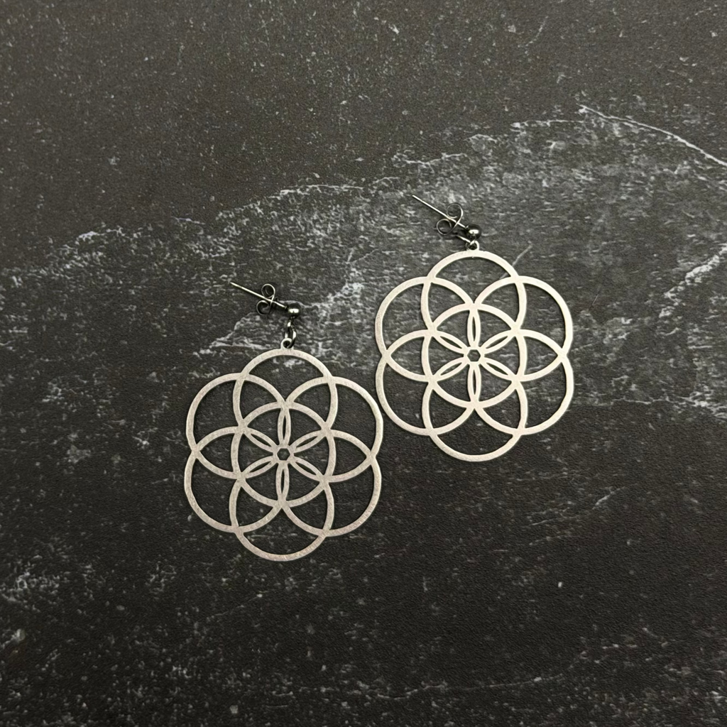 Stainless steel seed of life earrings on a dark textured surface