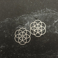 Stainless steel seed of life earrings on a dark textured surface
