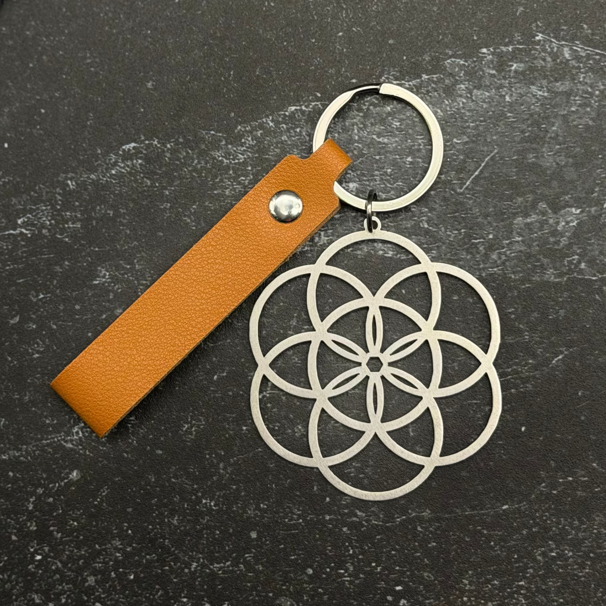 Stainless steel Keychain with geometric design and brown leather strap on a dark surface
