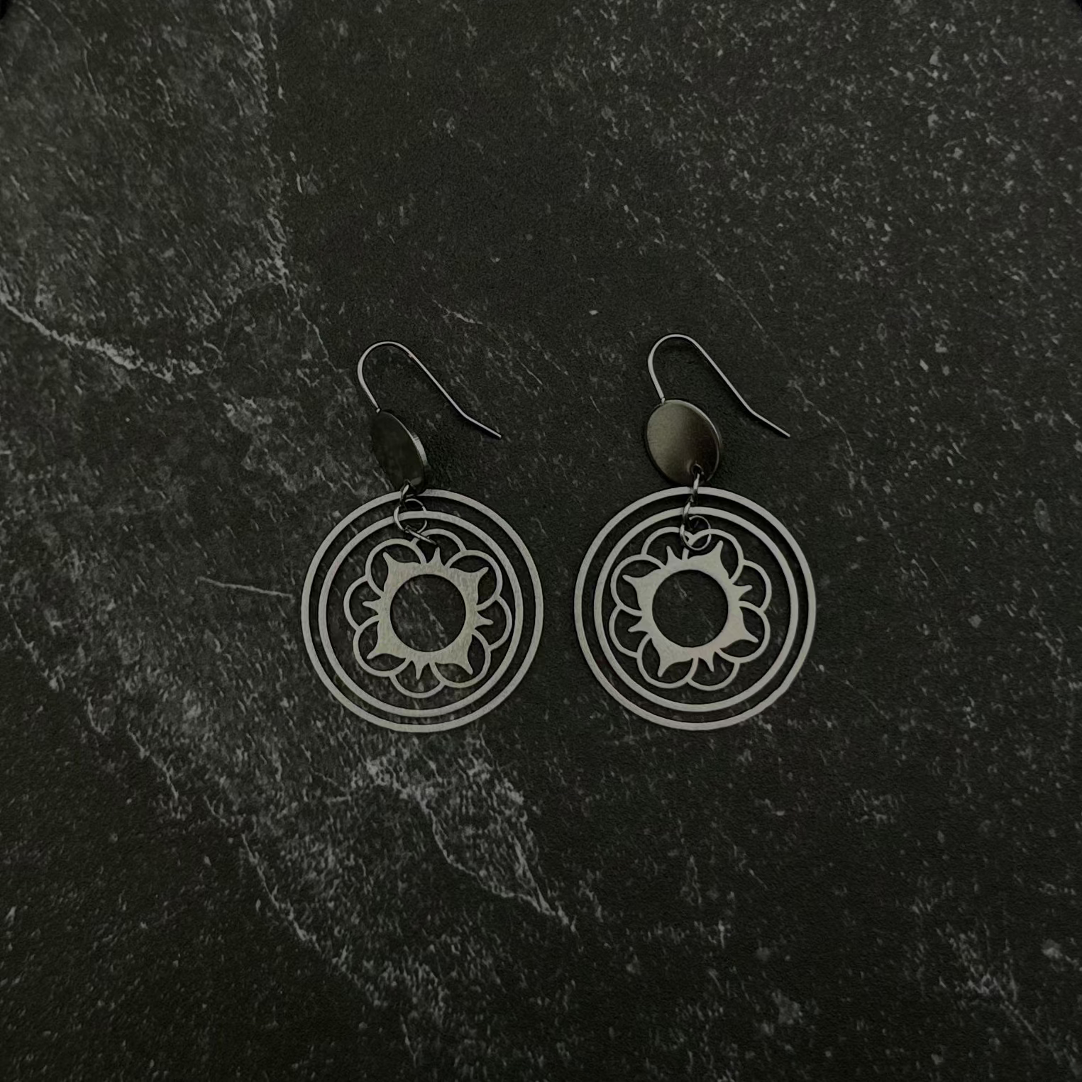 Pair of silver flower stacked circle earrings on a dark stone surface