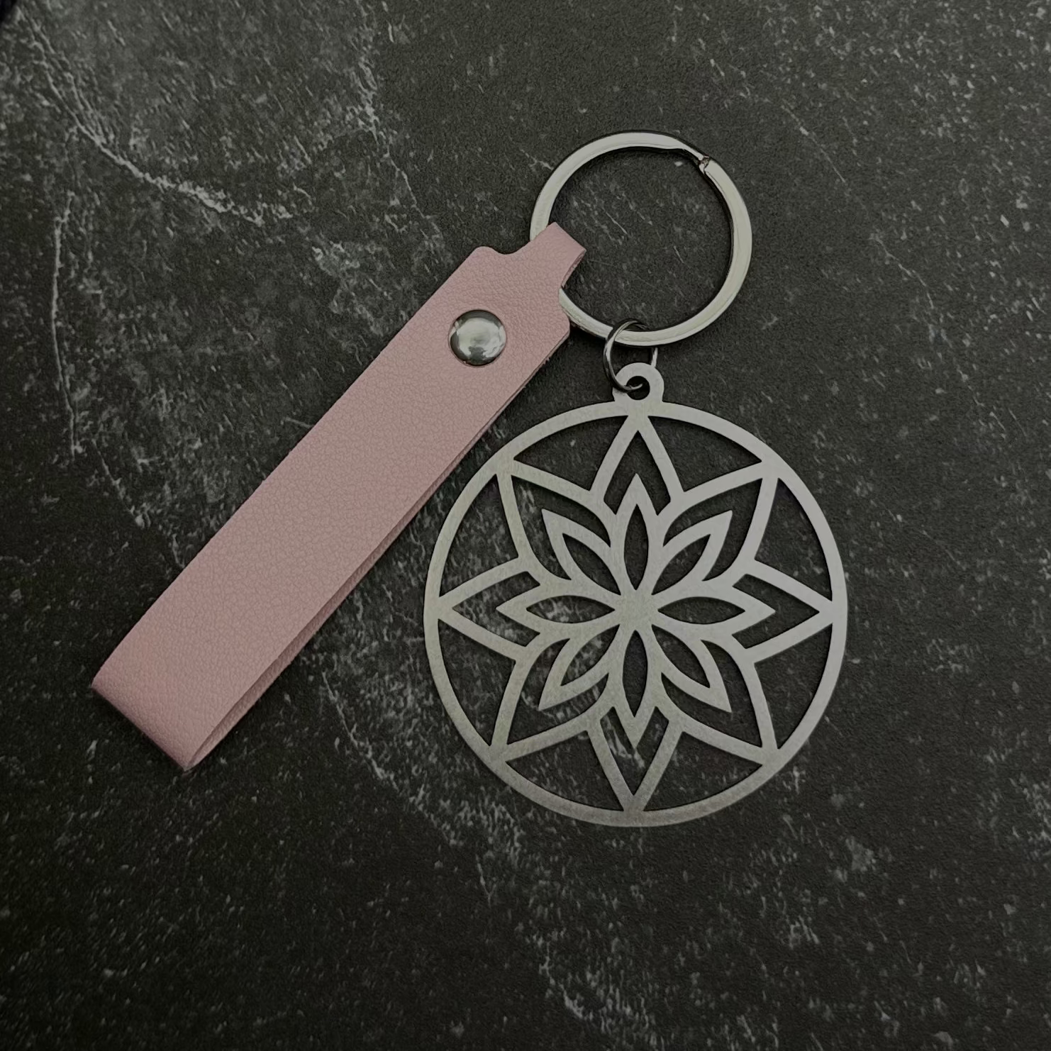 Floral design key chain with pink leather strap on a dark surface